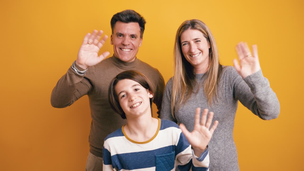 Famiglia felice che saluta e sorride alla fotocamera su sfondo giallo