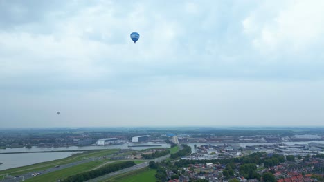 blue hot air balloon flying across hendrik-ido-ambacht town under clouds