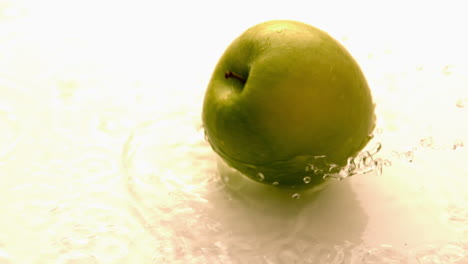 manzana cayendo y girando en la superficie blanca húmeda