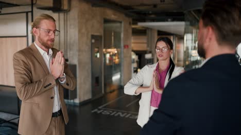 office workers doing group meditation during a break between work in a modern office. a girl in a white suit and a pink shirt, a guy in a brown jacket and a brunette guy in a blue jacket are engaged in meditation during a work break