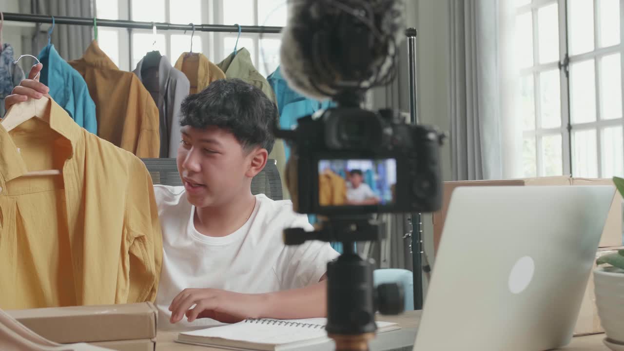 Asian Man Online Seller Recommending A Shirt And Recording Video By Camera While Using Computer For Selling Clothes At Home
