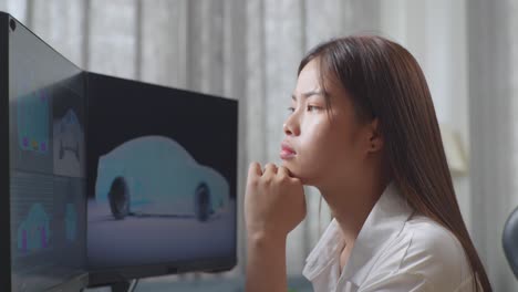 close up side view of asian female automotive designer thinking of idea then raising her index finger while working on 3d model of ev car on the desktop computers in the studio