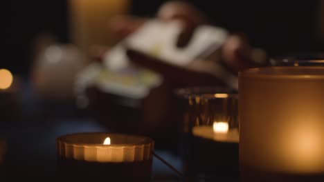 close up of woman shuffling or cutting cards for tarot reading on candlelit table with focus on foreground