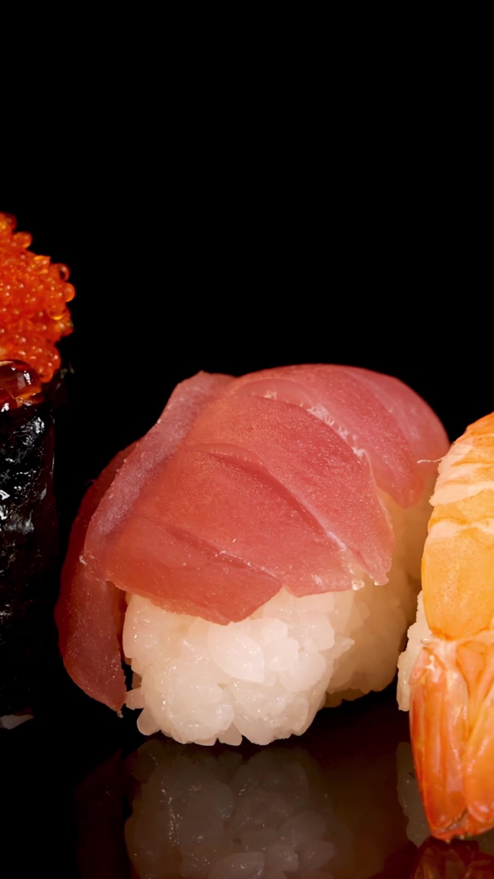 Una fluida panoramica laterale della telecamera rivela un vivace assortimento di sushi nigiri e sashimi su una superficie nera lucida, sotto un'illuminazione brillante e uniforme.