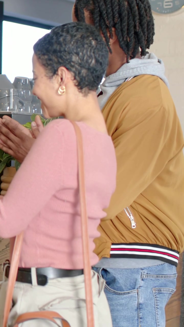 Vertical video: Approaching counter woman in pink leaning reaching man placing hand on back at cafe