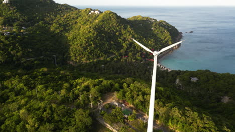 Toma-Aérea-En-órbita-De-Un-Molino-De-Viento-En-La-Isla-De-Koh-Tao-Con-Bahía-Y-Montañas-Verdes-En-El-Fondo-Al-Atardecer,-Tailandia