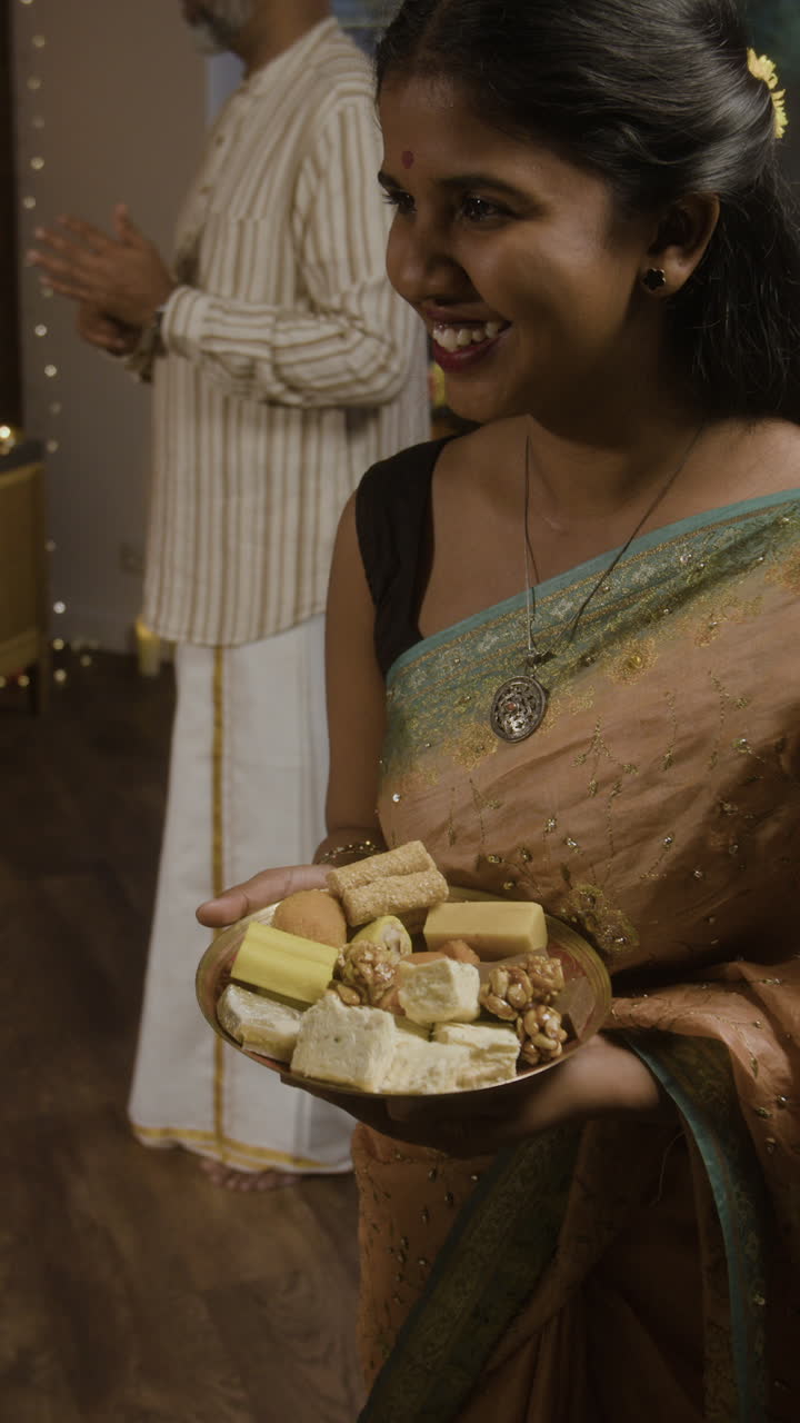 Donna in sari che tiene in mano un piatto di dolci indiani
