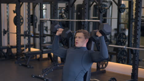 athlete in 30s performing dumbbell shoulder press, sitting on bench at gym