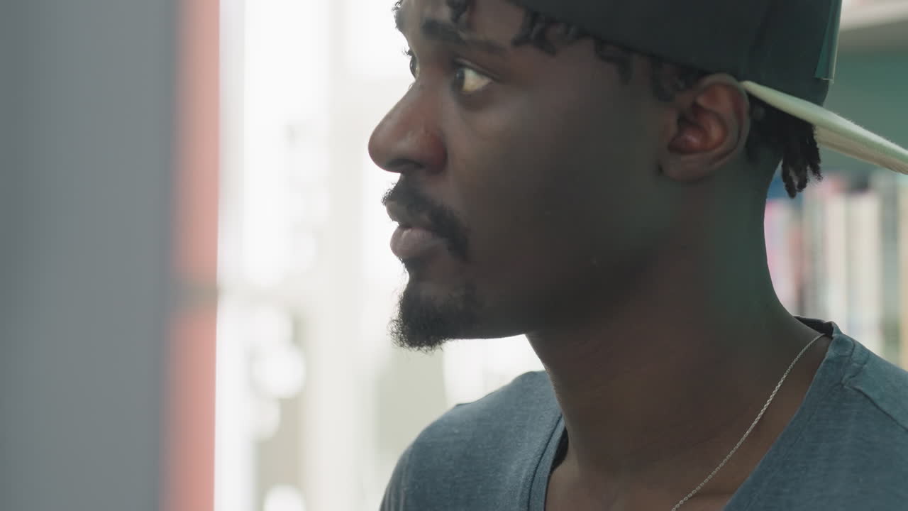 Close up side profile of college student in black cap sorting books on library shelf, with blurred background and focused expression, capturing calm academic atmosphere
