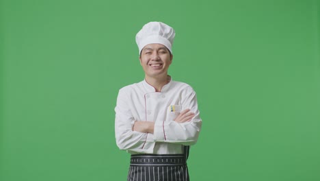 chef asiático sonriendo y cruzando los brazos a la cámara mientras está de pie en el estudio de fondo de la pantalla verde
