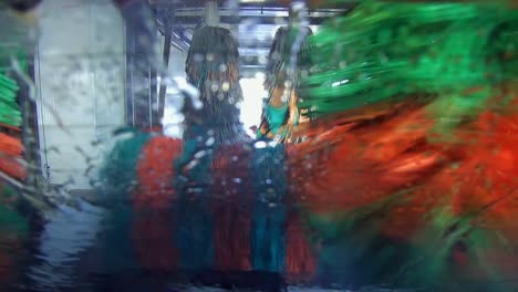 lavado automático de autos visto desde la parte trasera del vehículo moviéndose a través de la máquina coloridos rodillos salpicando agua en la ventana trasera