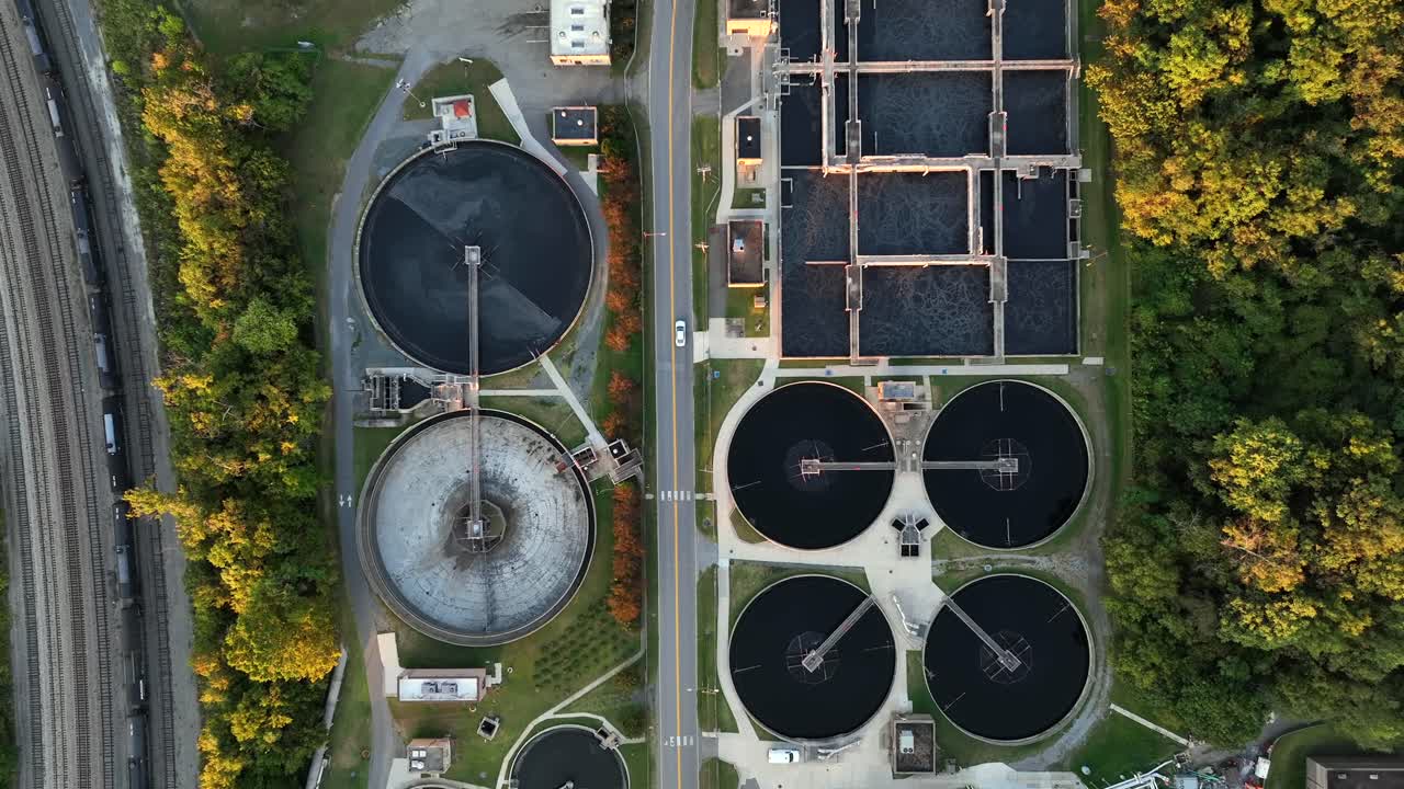 Sewage treatment plant with many circle pools and train on track. Sunset time in rural area of town. Lynchburg, Virginia. Aerial top down flyover. Peaceful scene