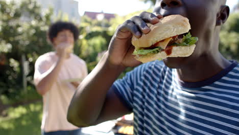 eating burgers outdoors, two multiracial male friends enjoying hangout together in garden