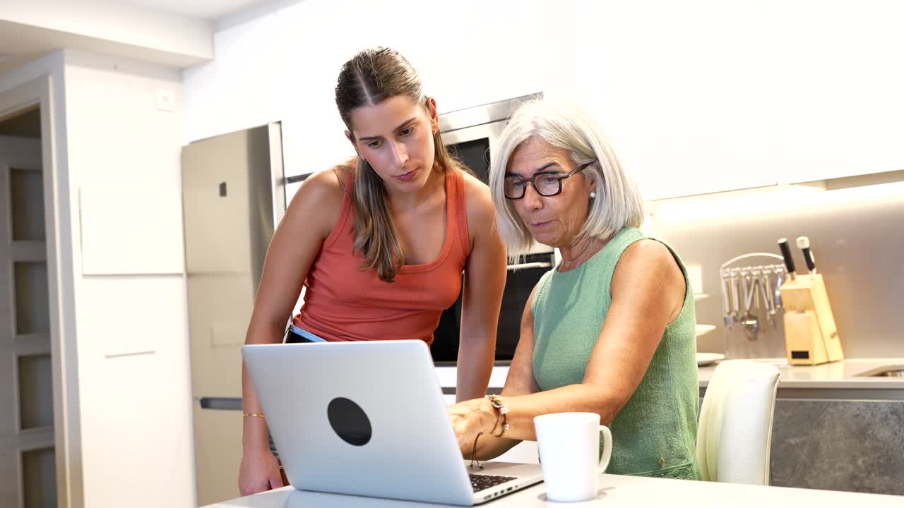 Oudere vrouw en kleindochter gebruiken laptop thuis