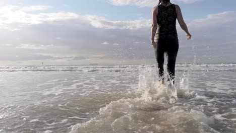 Tracking-Strandaufnahme-Eines-Mädchens,-Das-Im-Meer-Spazieren-Geht-Und-Mit-Den-Füßen-Die-Sanften-Wellen-Spritzt