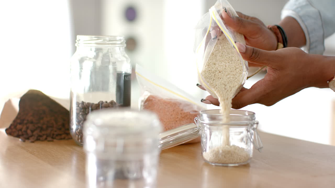 Pouring rice into glass jar, woman organizing pantry with various grains