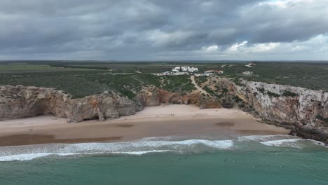 Wide-aerial-shot-of-surfers-waiting-in-the-waters-of-a-beautiful-bay-surrounded-by-cliffs