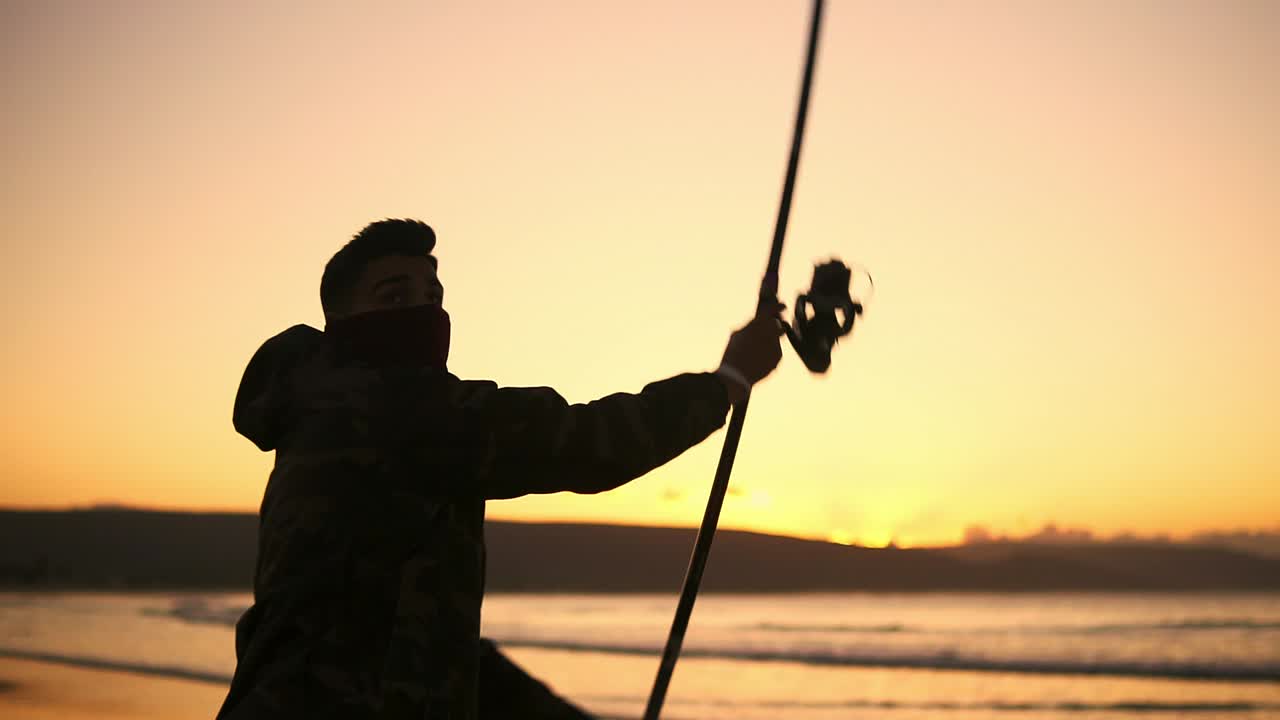 pescador contra la luz del atardecer lanzando una caña de pescar hacia la orilla del mar