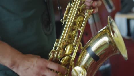 close-up of a musician's hands playing a saxophone with an upright bass in the background