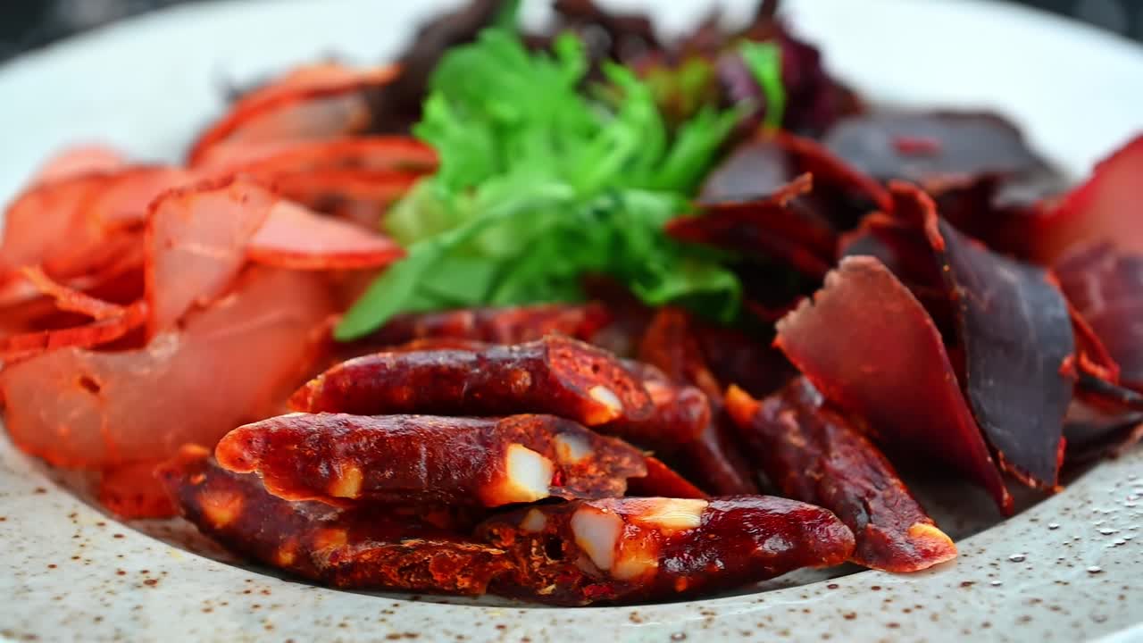 Diversi tipi di carne serviti su un piatto con verdure. Fette di carne e snack secchi su un piatto, insieme a verdure fresche e alimenti rossi, pronti da mangiare