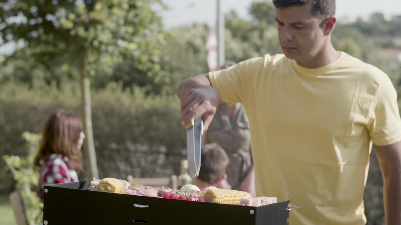 hombre serio girando carne y salchichas en la parrilla de barbacoa