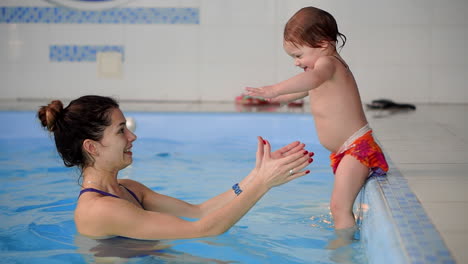 baby in the pool jumping from the side into the water and swims to his mother in slow motion