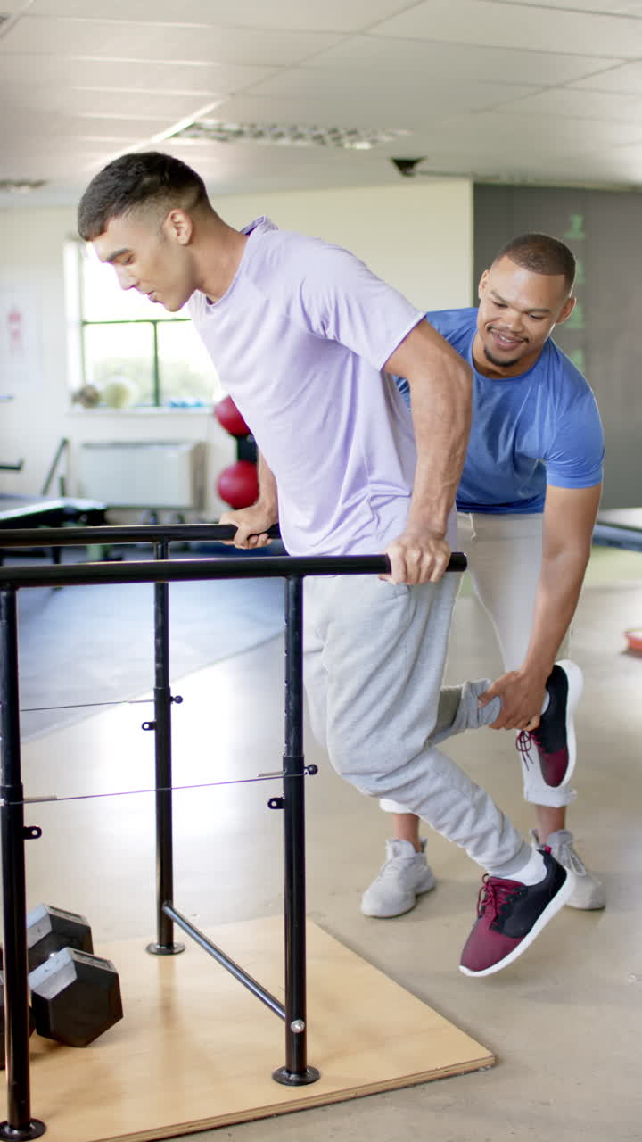 Vertical video: Exercising on parallel bars with therapist, man with disability in rehabilitation th