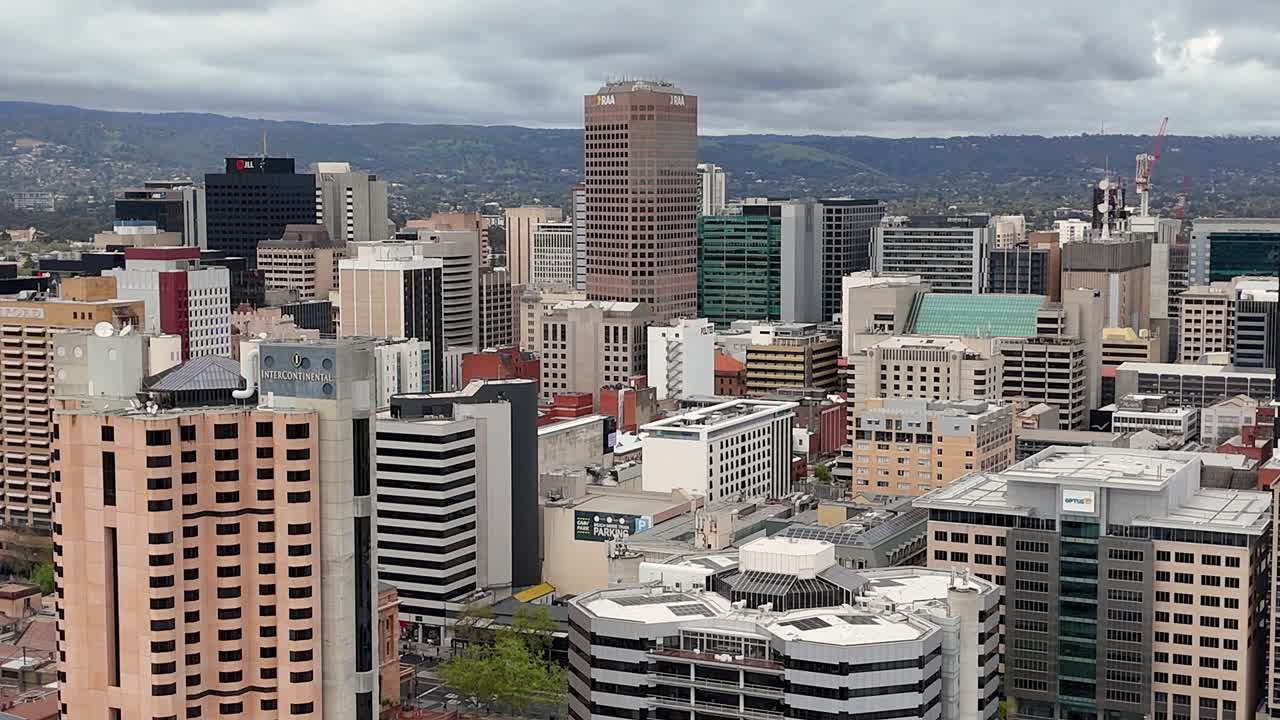 Aerial view of the Adelaide CBD buildings and skyscrapers. This video features the Adelaide Hills in the distance, office buildings, and a cloudy sky. Adelaide is the capital of South Australia.