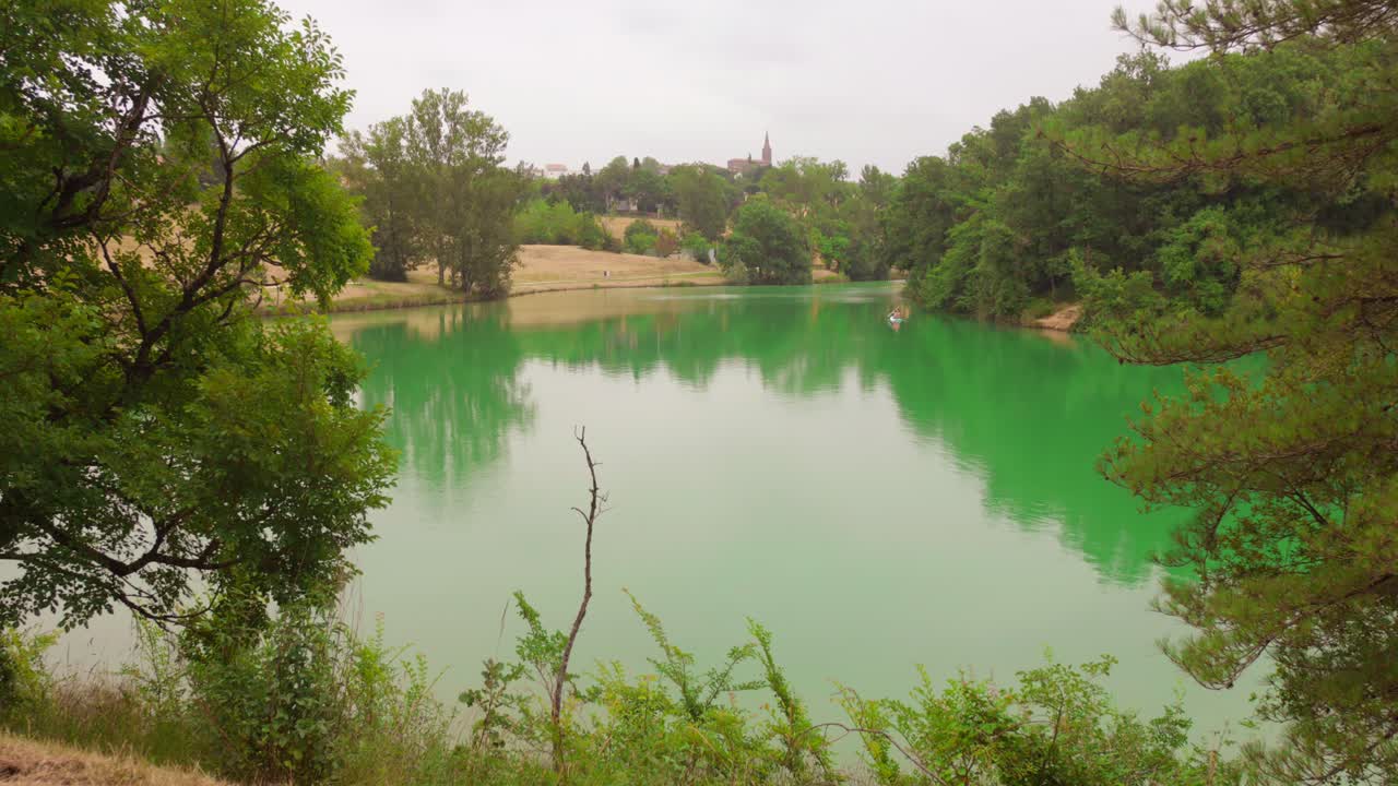 Static shot of beautiful Lac de L'Orme Blanc" (a lake) in Caraman, France with lush foliage in foreground during daytime
