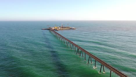 aerial over a long oil pier extending to a small island off the shore of mussel shoals rincon beach santa barbara california 1