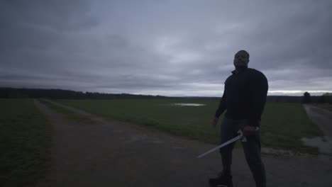 Modern-Black-Swordsman-Warrior-Awaiting-Battle-Opponent-in-Open-Field-Under-Grey-Sky,-Europe,-4K-|-Muscular,-Intimidating,-Shadow,-Figure,-Blurry,-Dark-Clothes,-Powerful,-Tired,-Wobbly,-Winded