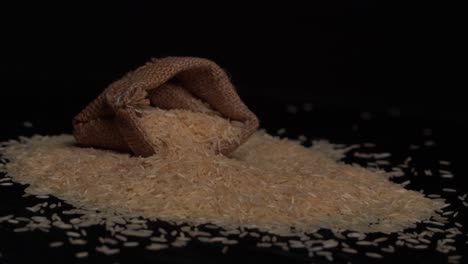 close up shot of raw basmati white rice in a gunny bag on falling on black surface