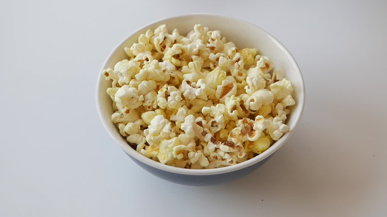 Uma mão alcança uma tigela de pipoca