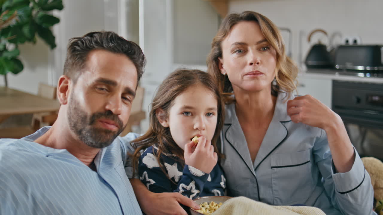 Happy family watching tv eating popcorn on sofa in light living room closeup