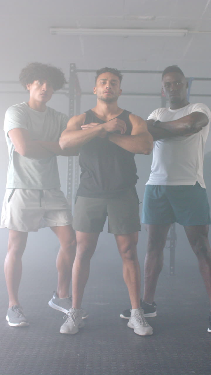 Vertical video: Standing confidently, three men posing with crossed arms in gym