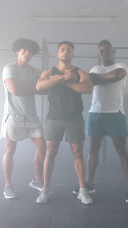 vertical video: standing confidently, three men posing with crossed arms in gym