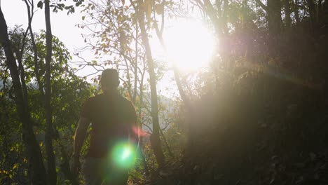 joven caminando por el sendero del bosque llegando al pico. mochilero masculino caminando por la montaña al atardecer con la luz de la lente. excursionistas caminando en el bosque de otoño con fondo cinematográfico de amanecer. cámara lenta