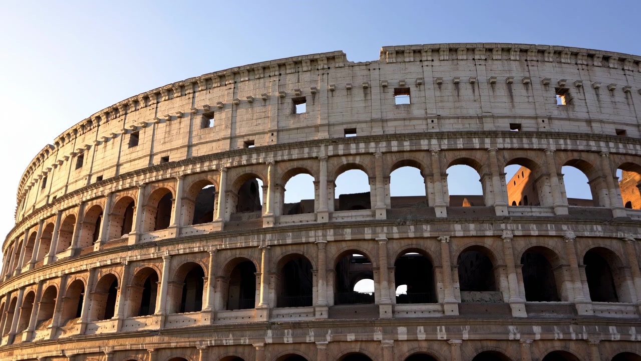 Façade du Colisée baignée de soleil au coucher du soleil, révélant ses arches superposées, ses tons chauds de travertin, des ombres dramatiques et un ciel clair.