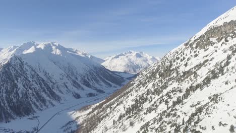 Aerial-shot-of-a-mountain-valley-with-settlement-and-road-placed-between-steep-alpine-slopes