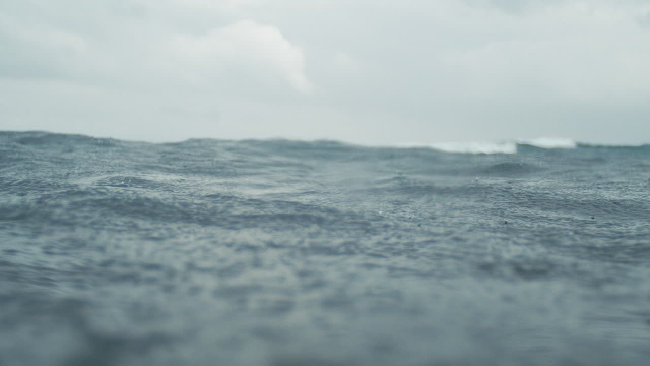 Raindrops fall in slow motion creating dynamic textures on ocean surface