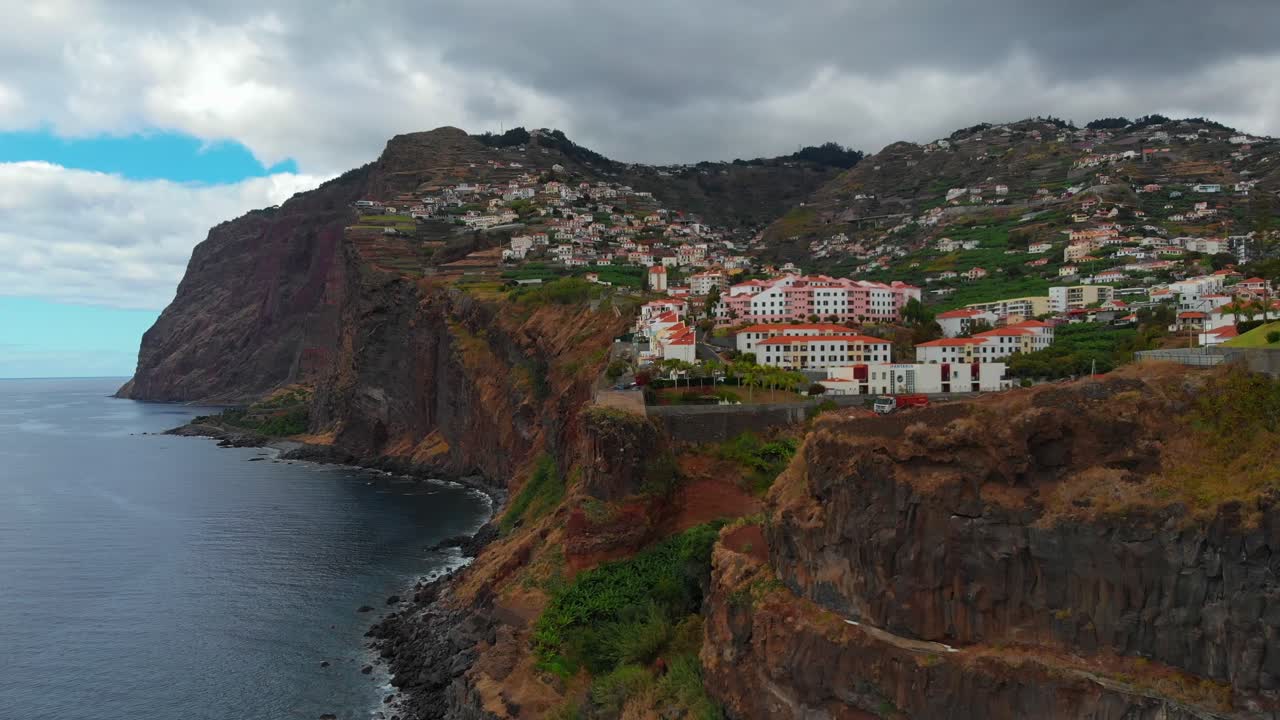 Vista aérea de íngremes penhascos vulcânicos e casas na encosta com vista para o Oceano Atlântico perto de Câmara de Lobos, Madeira, Portugal, mostrando o litoral acidentado, as encostas em socalcos e a paisagem da ilha