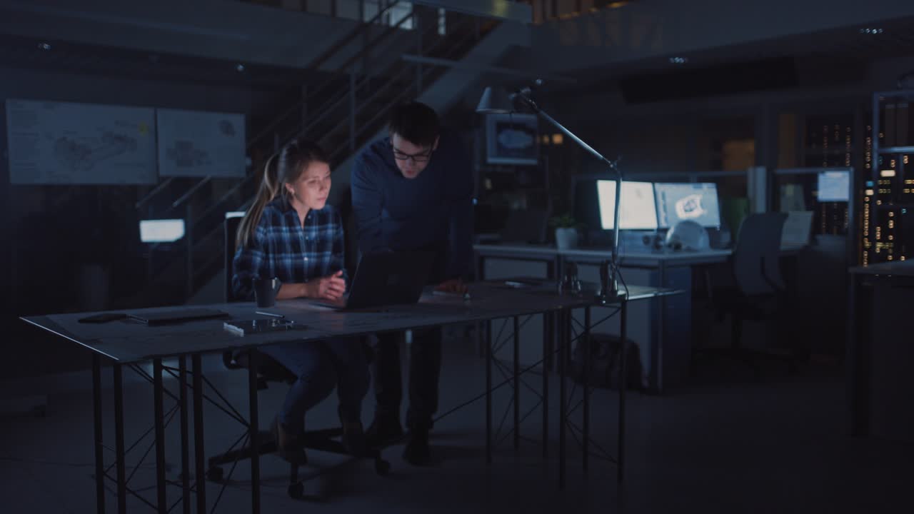 Industrial Engineering Facility: Female Engineer Working on Desktop Computer, Project Manager Stands Beside and Explains Specifics of the Task and Project Details. Working Late on Engine Prototype
