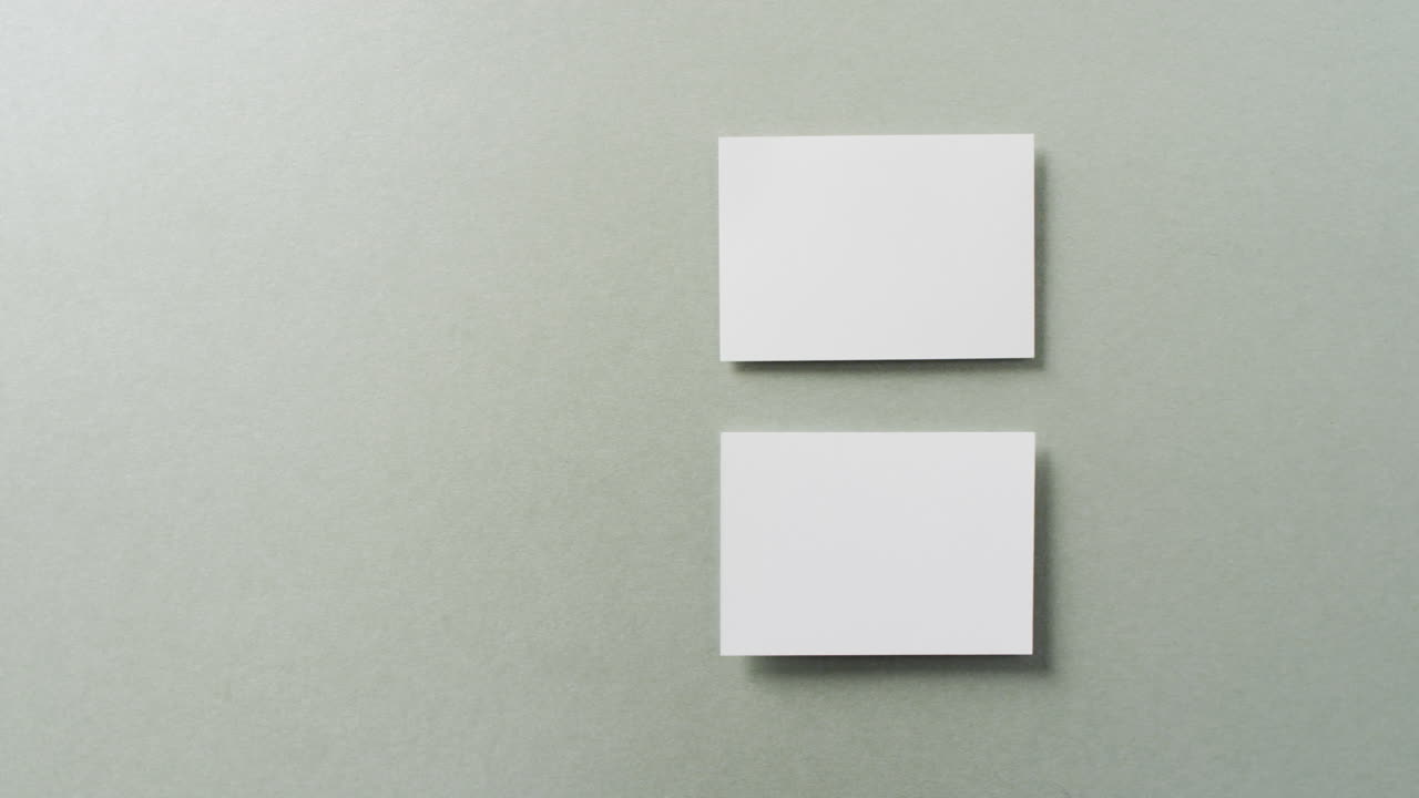 Overhead view of two white business cards arranged on grey background, copy space, slow motion