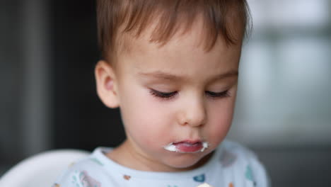 charming caucasian baby boy eating yogurt. close up portrait of a toddler having healthy meals.