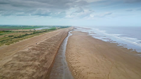 Aerial-video-footage-of-a-coastal-beach-scene-with-ocean,-sand-dunes-and-crashing-waves