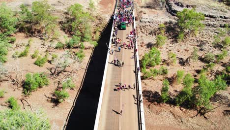 aerial view of children leading crowds over the bridge across the victoria river in the freedom day festival march in the remote community of kalkaringi, northern territory, australia