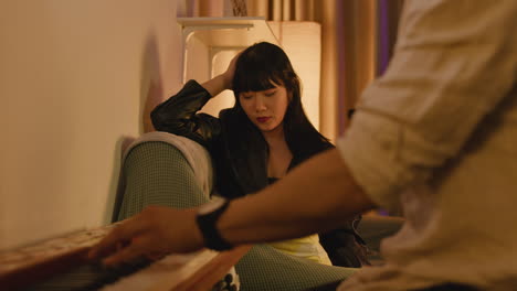 asian woman sitting on couch while man plays piano