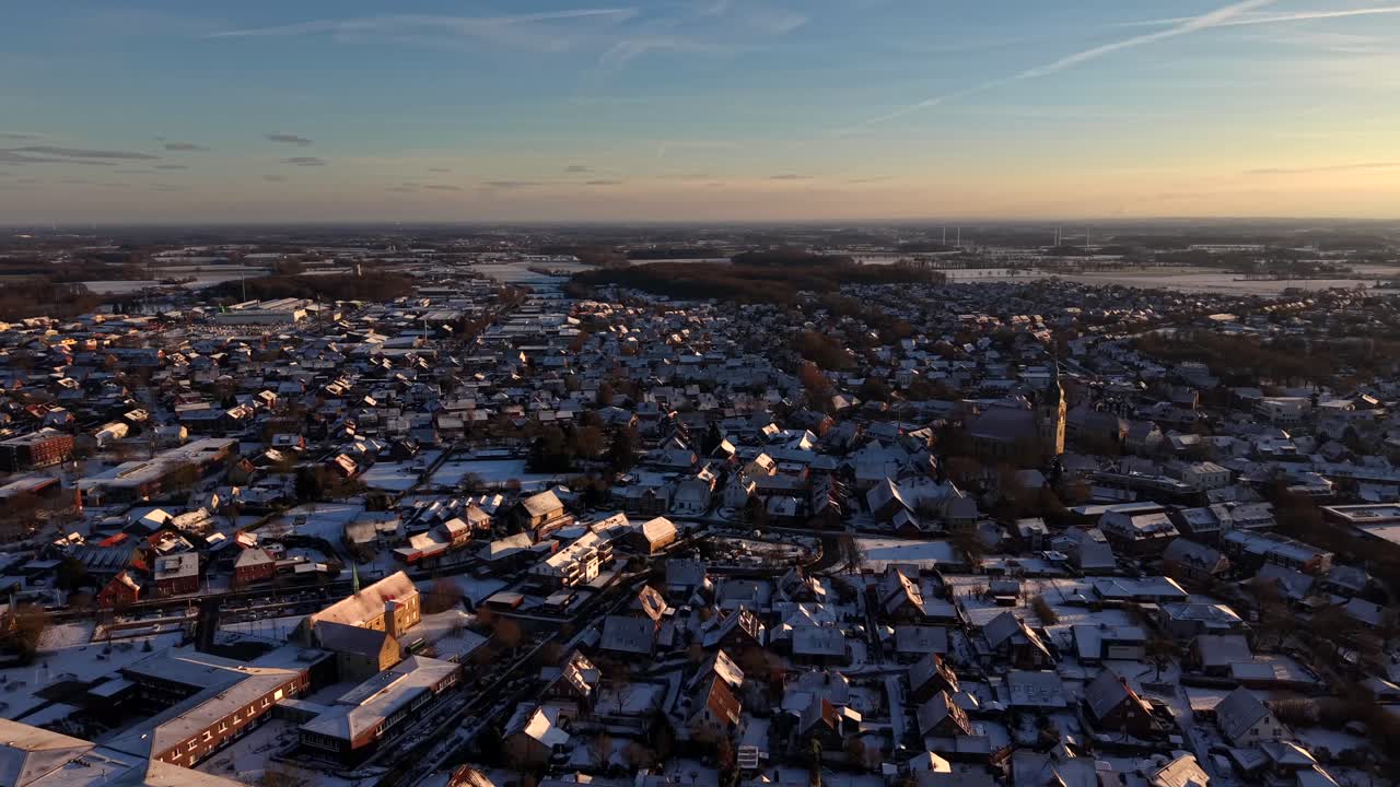 Lotnicze ujęcie ogólne ośnieżonego miasteczka w Ameryce w czasie złotej godziny. Zabytkowa wieża kościelna w ośnieżonej wiosce. Szeroki kąt. Czas zachodu słońca. Oddalone tereny rolne. Spokojna i cicha dzielnica mieszkalna