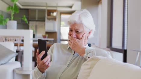 Ältere-Frau-Führt-Einen-Videochat-Auf-Dem-Smartphone,-Während-Sie-Zu-Hause-Auf-Der-Couch-Sitzt