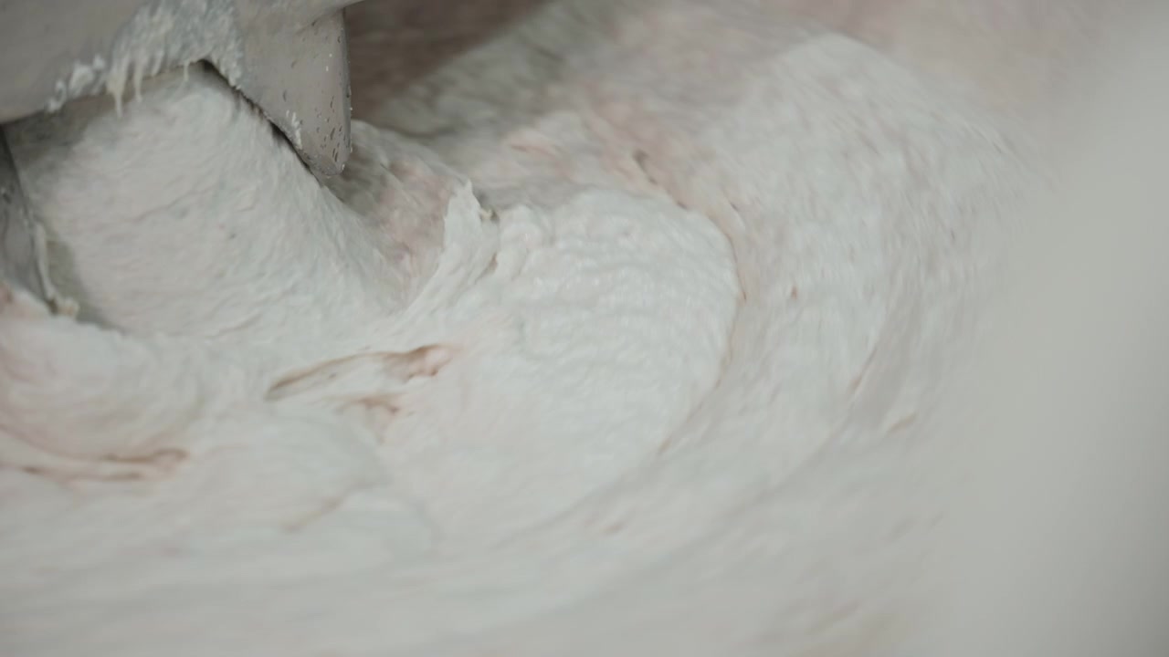 Lys røre vispes rundt en metallpadle i en automatisert mikser under hygienisk matproduksjon.